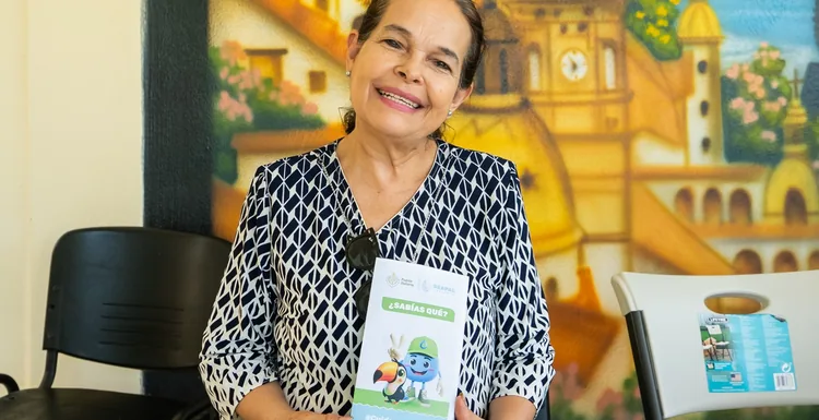 A woman holds a SEAPAL information leaflet while seated in front of a Puerto Vallarta mural.